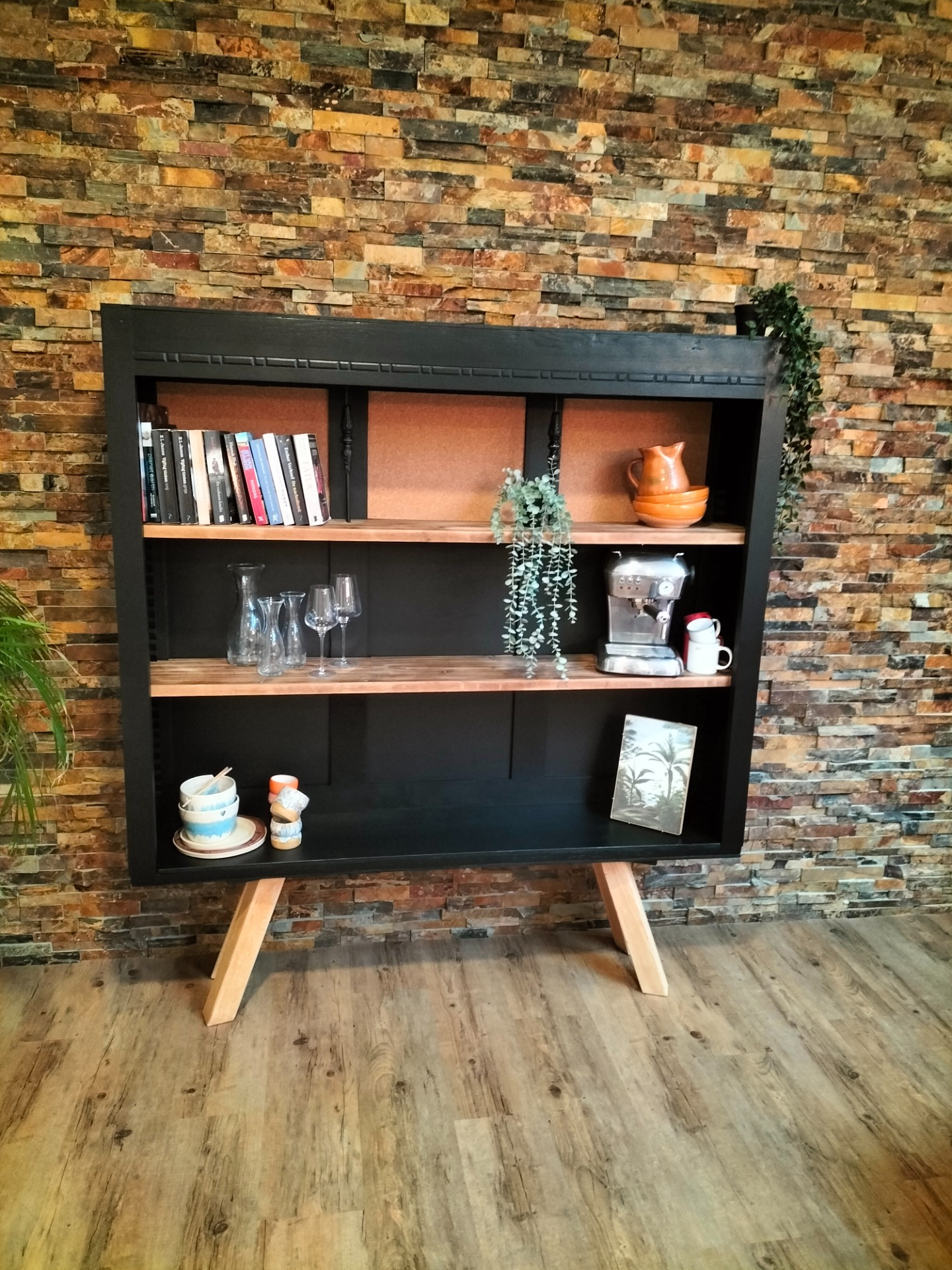 Donkere houten kast met boeken, glazen, koffiezetapparaat en vaas tegen kleurrijke stenen muur. Displaykast. Boekenkast. Vintage. interieur. Studio interieur. Podcast studio.
